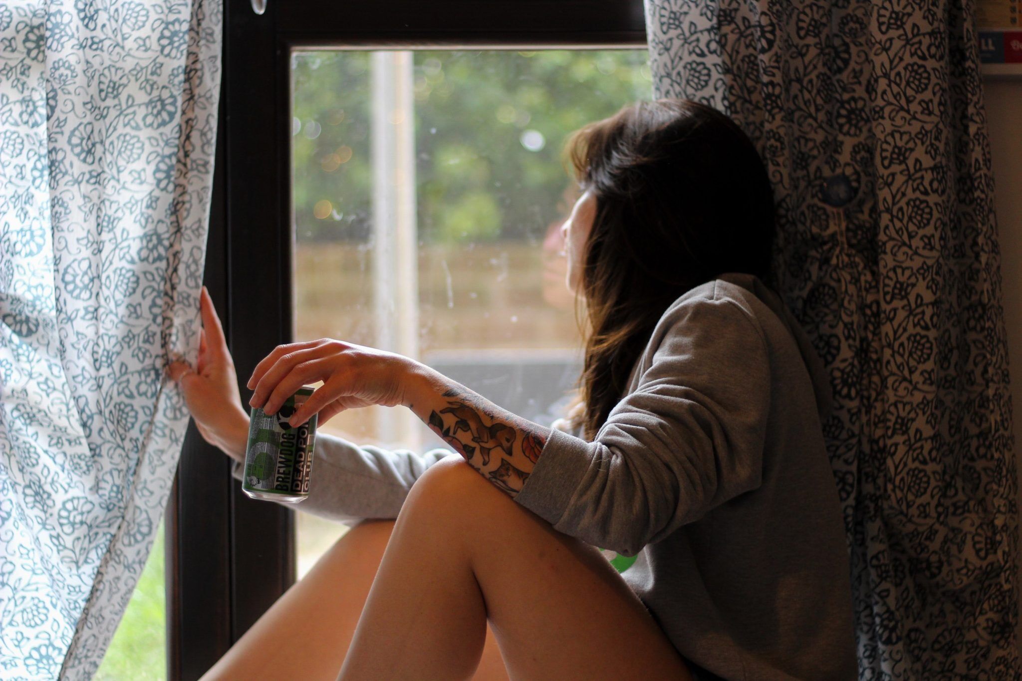 woman holding beer can and looking out the window