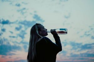 woman drinking from bottle at sunset, signs of alcoholism