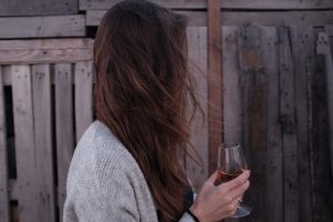 woman drinking wine by fence, signs of alcoholism