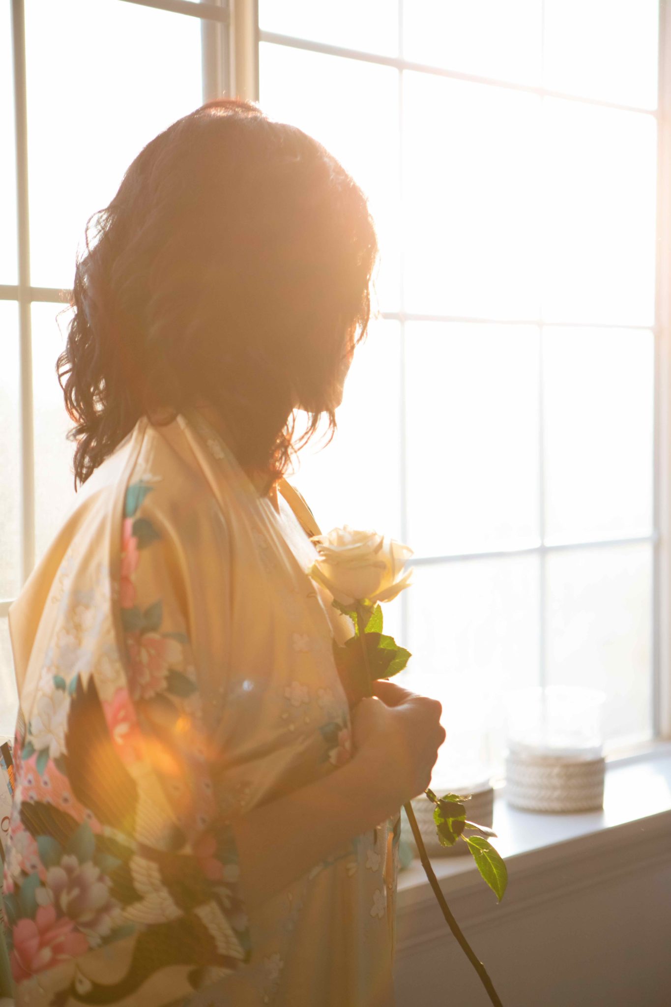 woman standing by window clutching flower