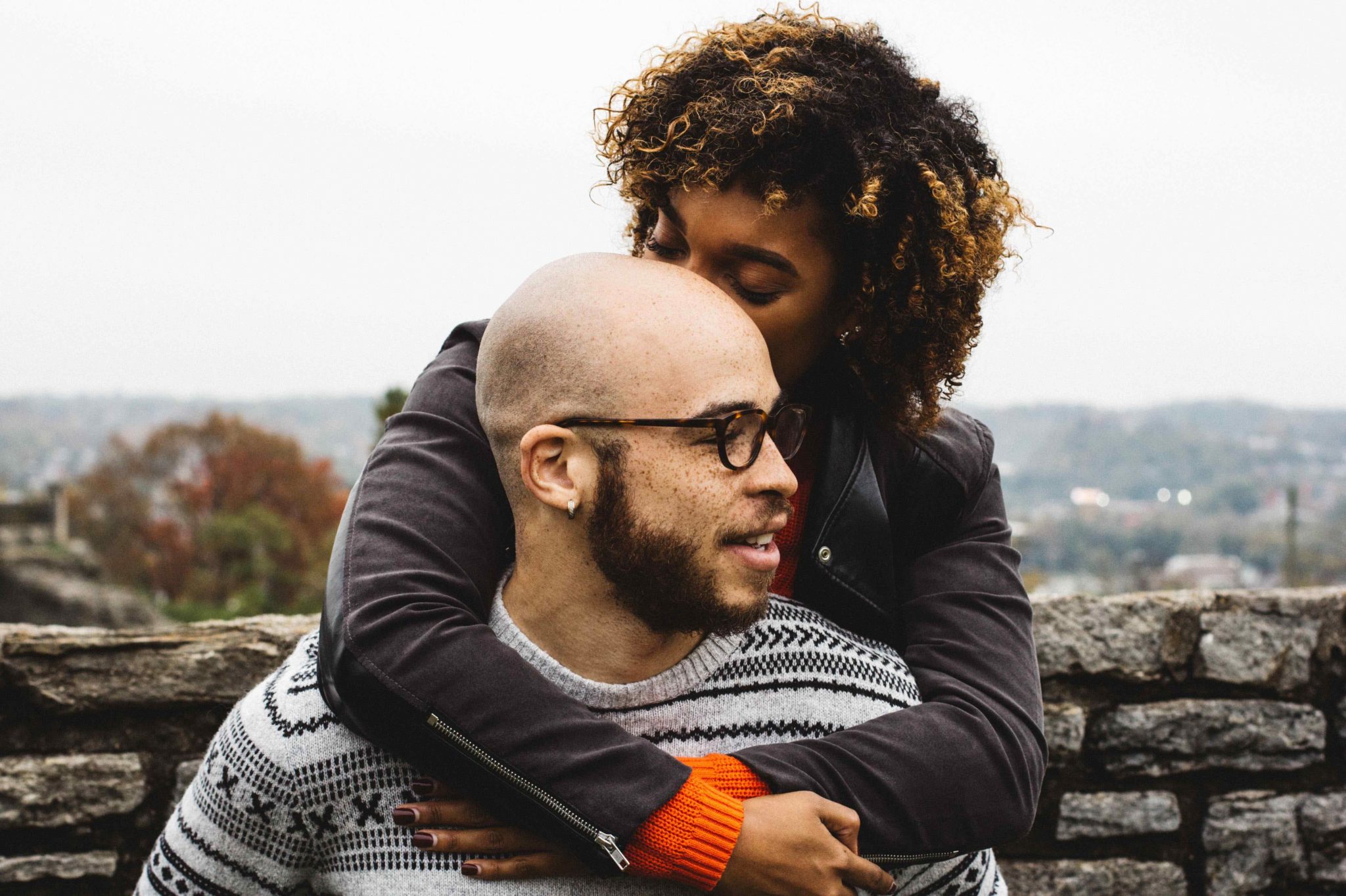 woman kissing man's head while hugging him from behind