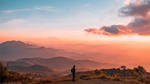 man standing among mountains at sunset