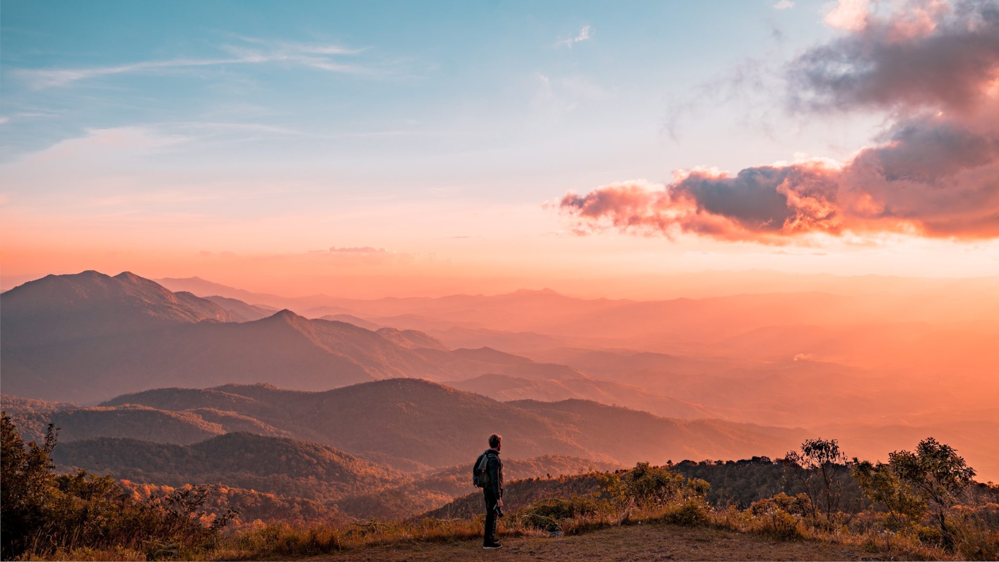 man standing among mountains at sunset