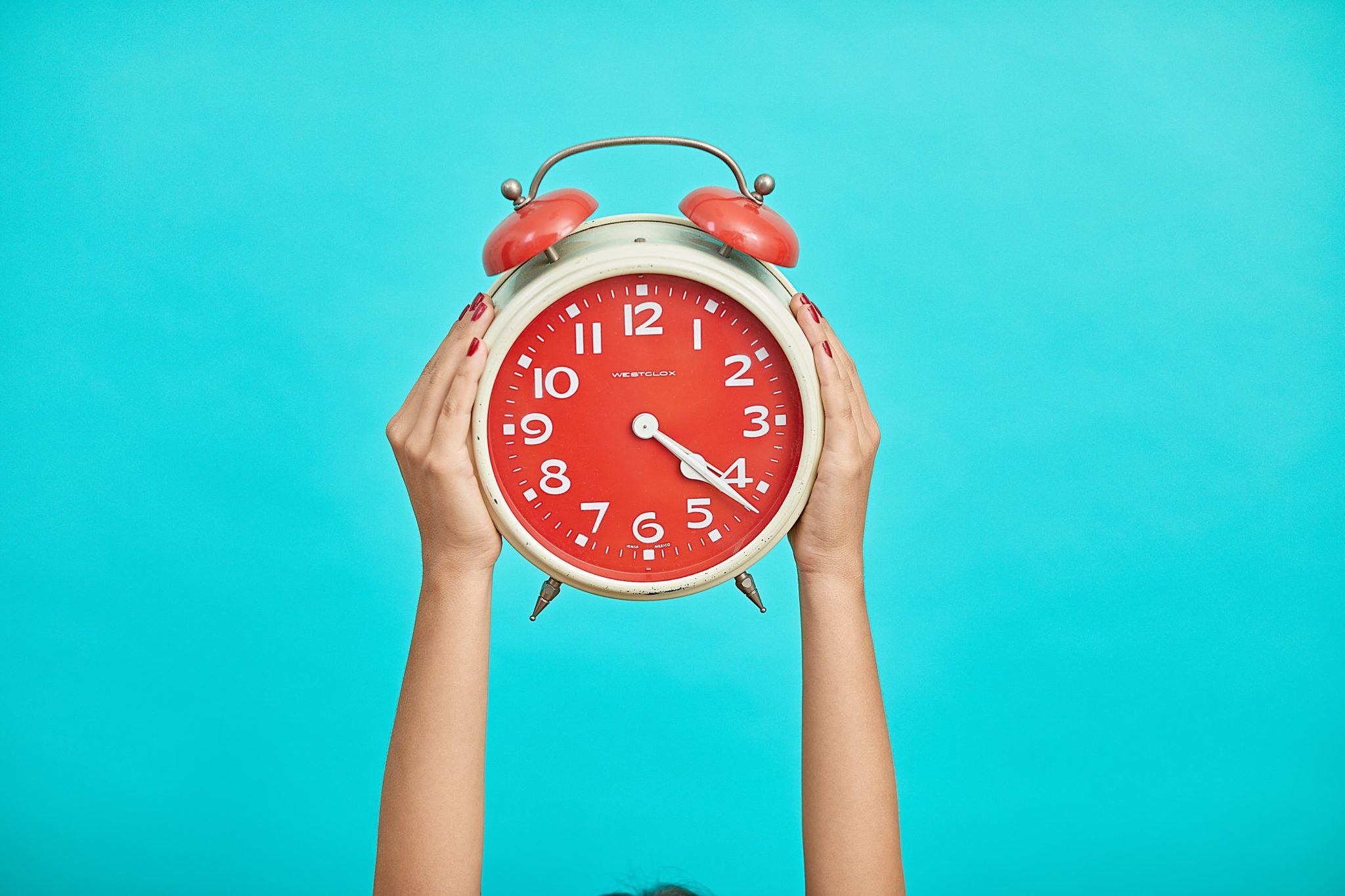 hands holding alarm clock on blue background