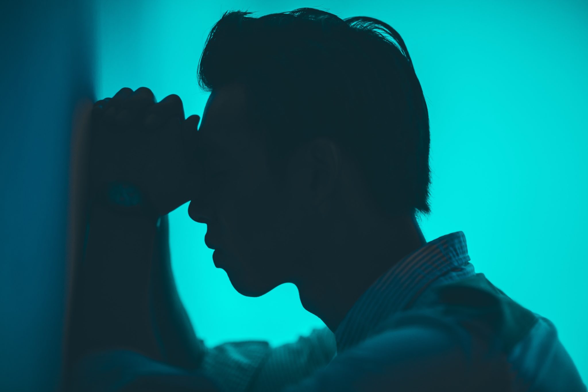 man leaning against the wall with his hands pressed against his temples