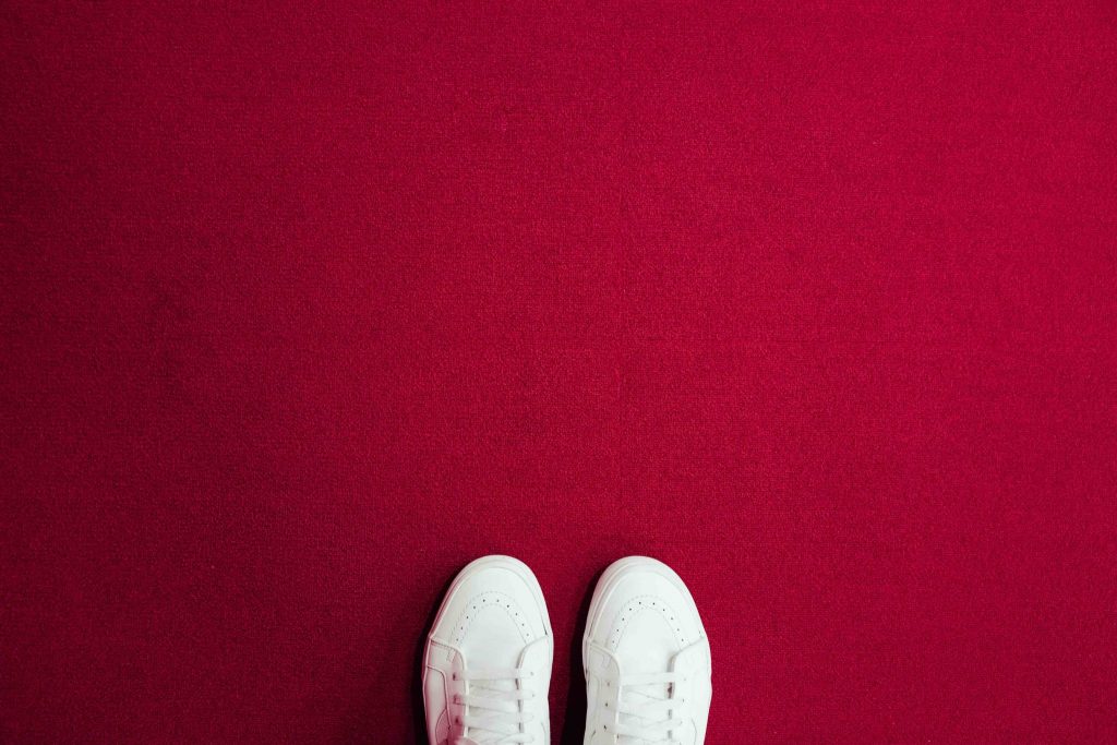 feet in white shoes on red carpet