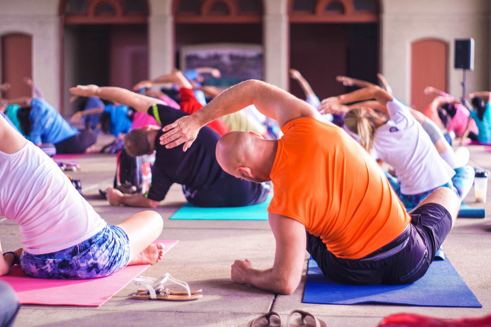 rows of people in bright clothing stretching on yoga mats
