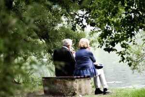 older couple sitting on a bench overlooking a lake