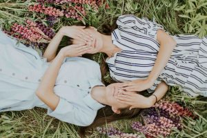 two women lying on the grass covering each others eyes