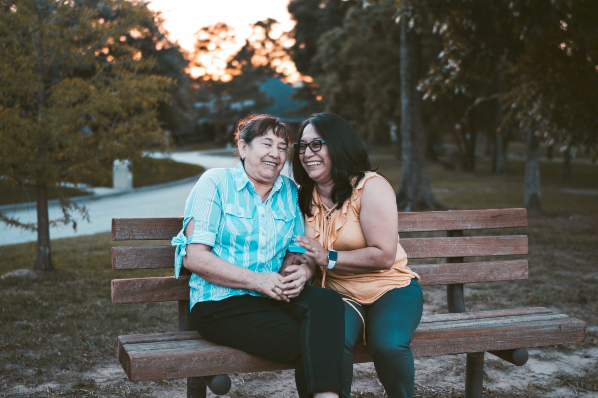 two older women sitting on a bench and laughing together