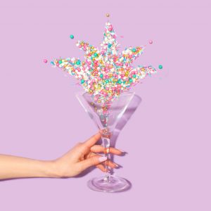 hand holding glass full of colorful candy with purple background