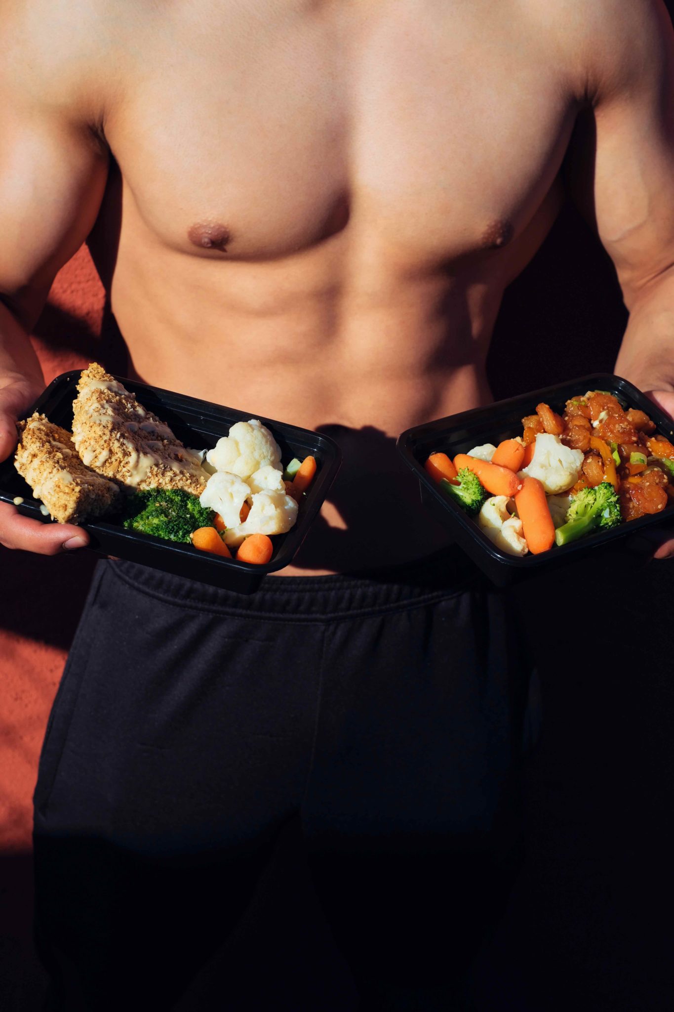 shirtless man with six pack abs holding plates of vegetables
