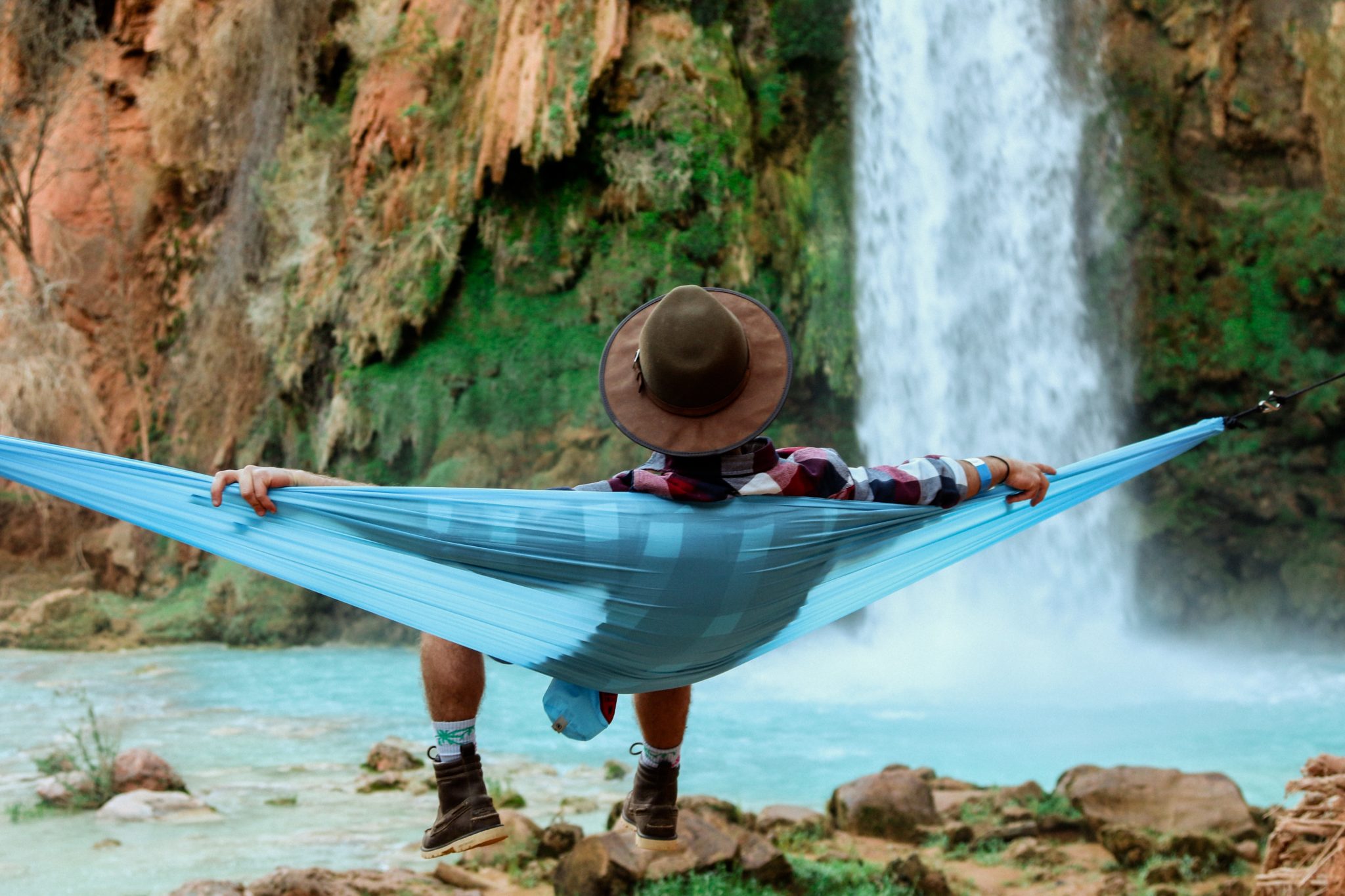 man in a hammock looking at a waterfall complacent