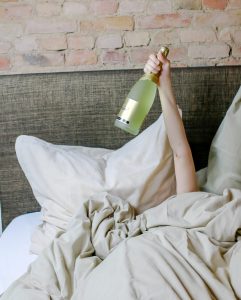 arm holding a wine bottle from under the bed covers