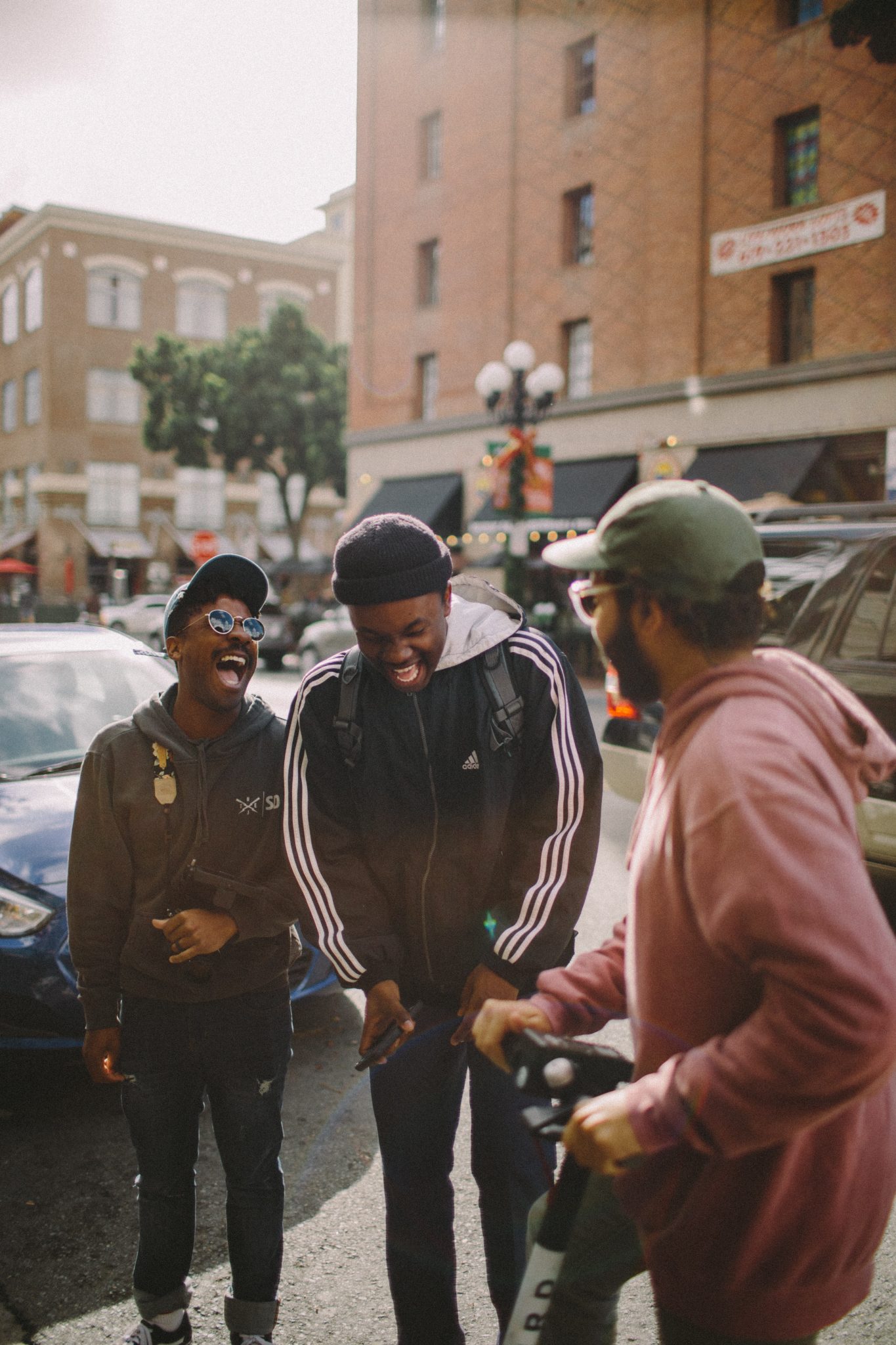 three men with scooters laughing on a city street