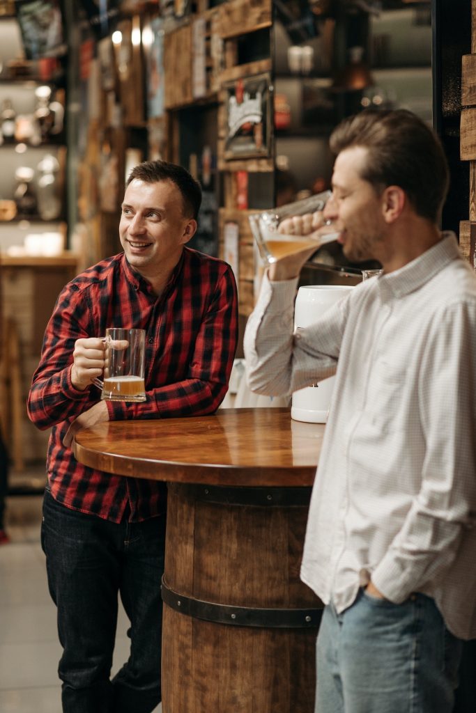 two men standing at a table drinking beer