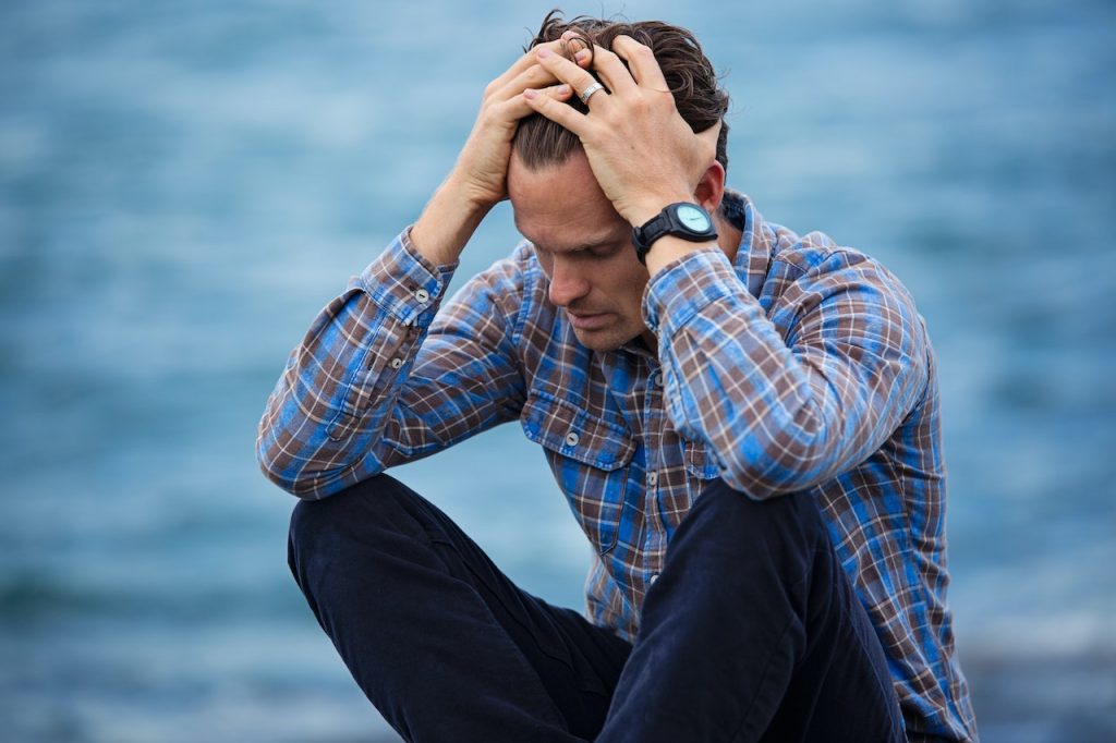 Man sitting by water holding his head