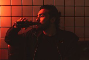 red lit photo of man drinking beer alone at a bar