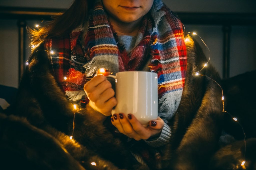 person holding hot mug wearing christmas lights