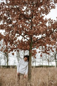 man leaning against autumn tree with dead leaves