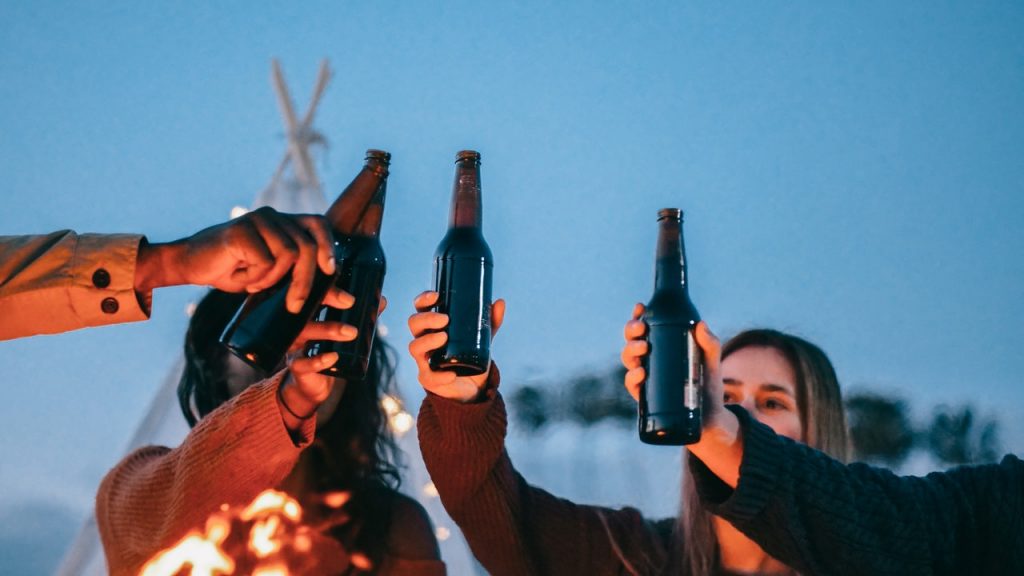 friends hoisting beer bottles over a campfire
