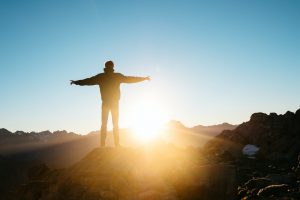 person standing open armed on hill facing the sun