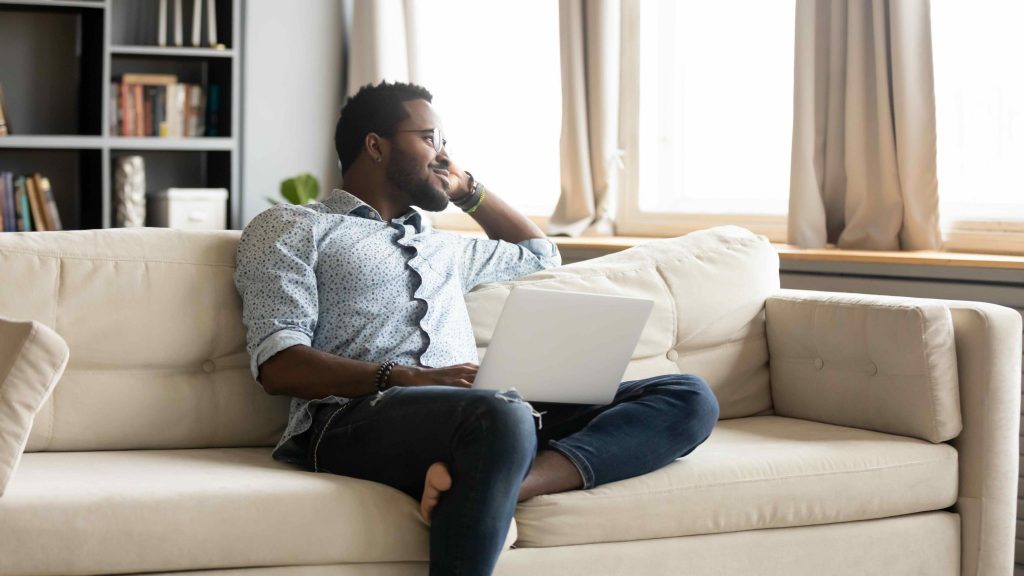 man sitting on couch with laptop pondering a positive change