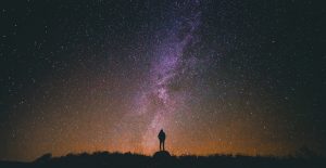 person looking up at a bright galaxy in the night sky