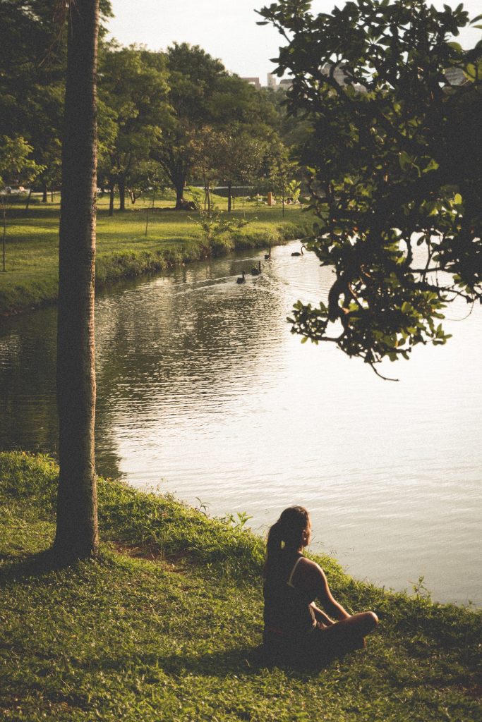 person meditating by a lake in the park