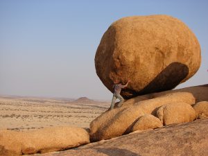 man posing beneath large boulder