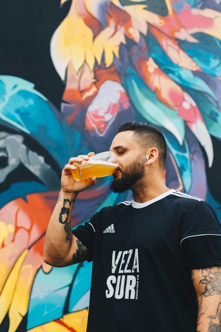 man drinking beer in front of colorful wall