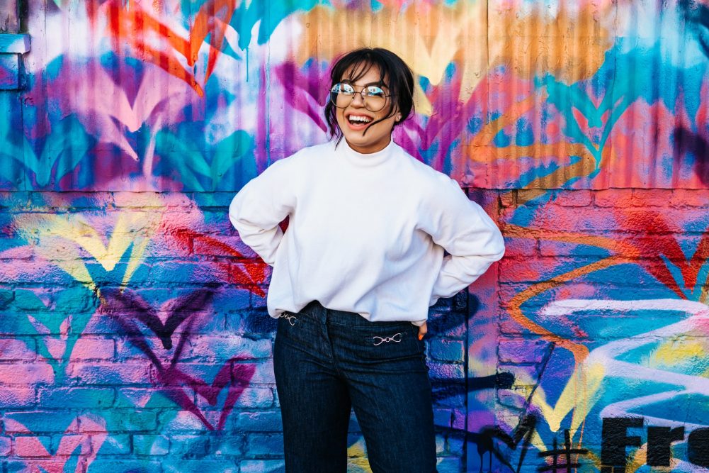 woman smiling and standing by a colorful wall