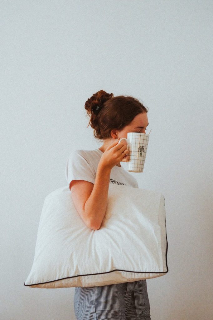 woman holding pillow hiding face behind coffee cup