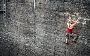 woman with climbing gear scaling a gray wall