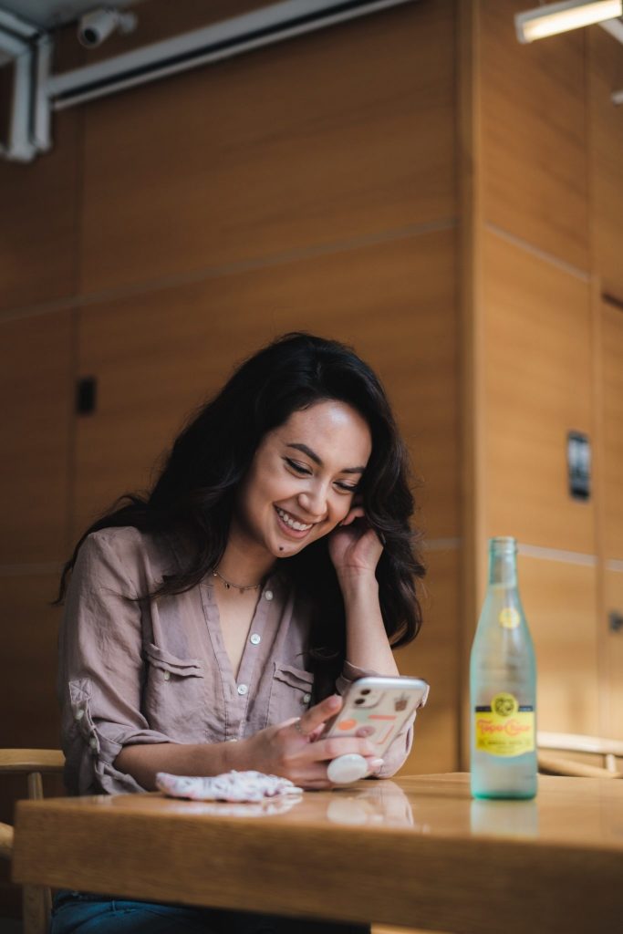 woman sitting at table with drink using smartphone