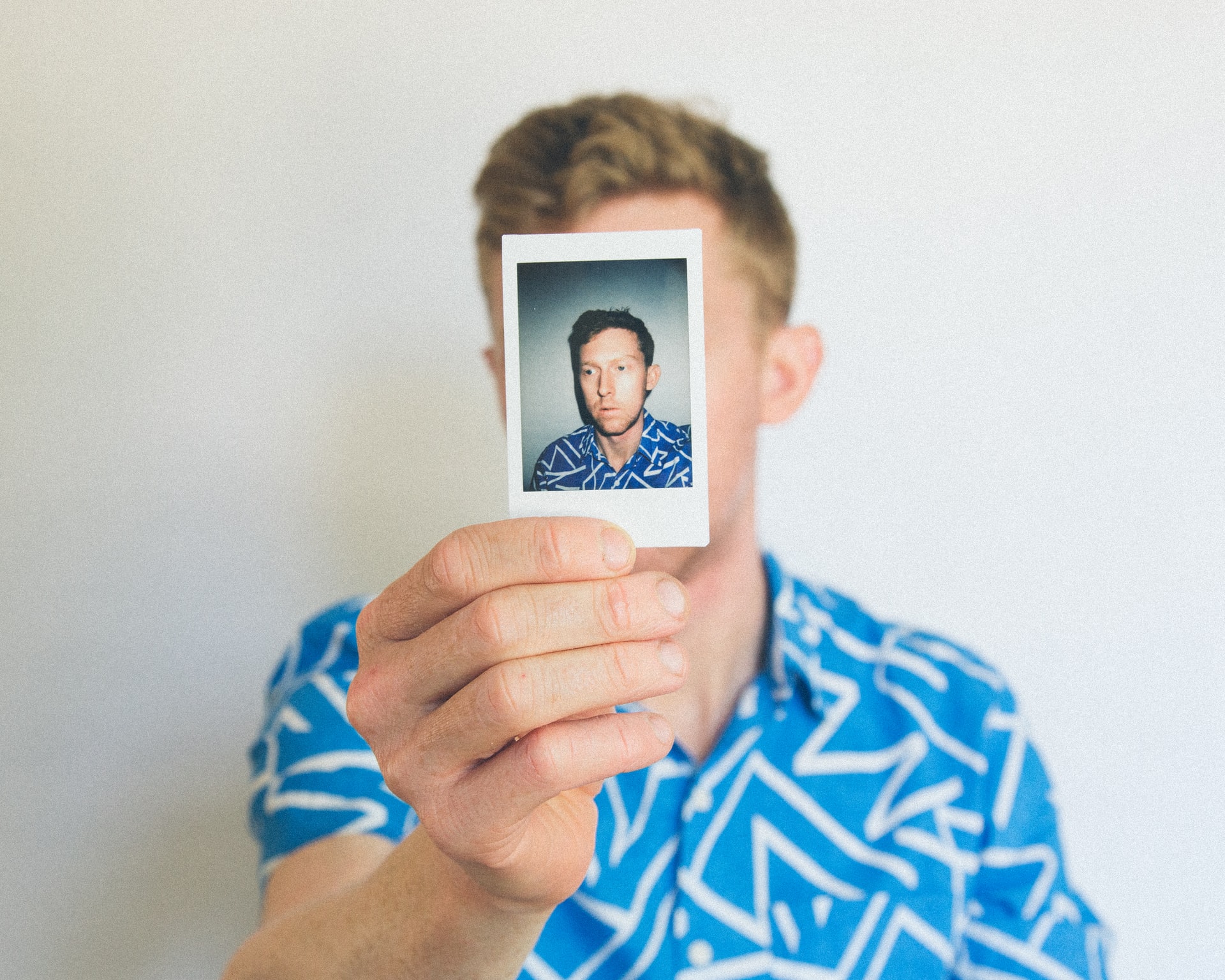 man holding polaroid picture of himself in front of his face