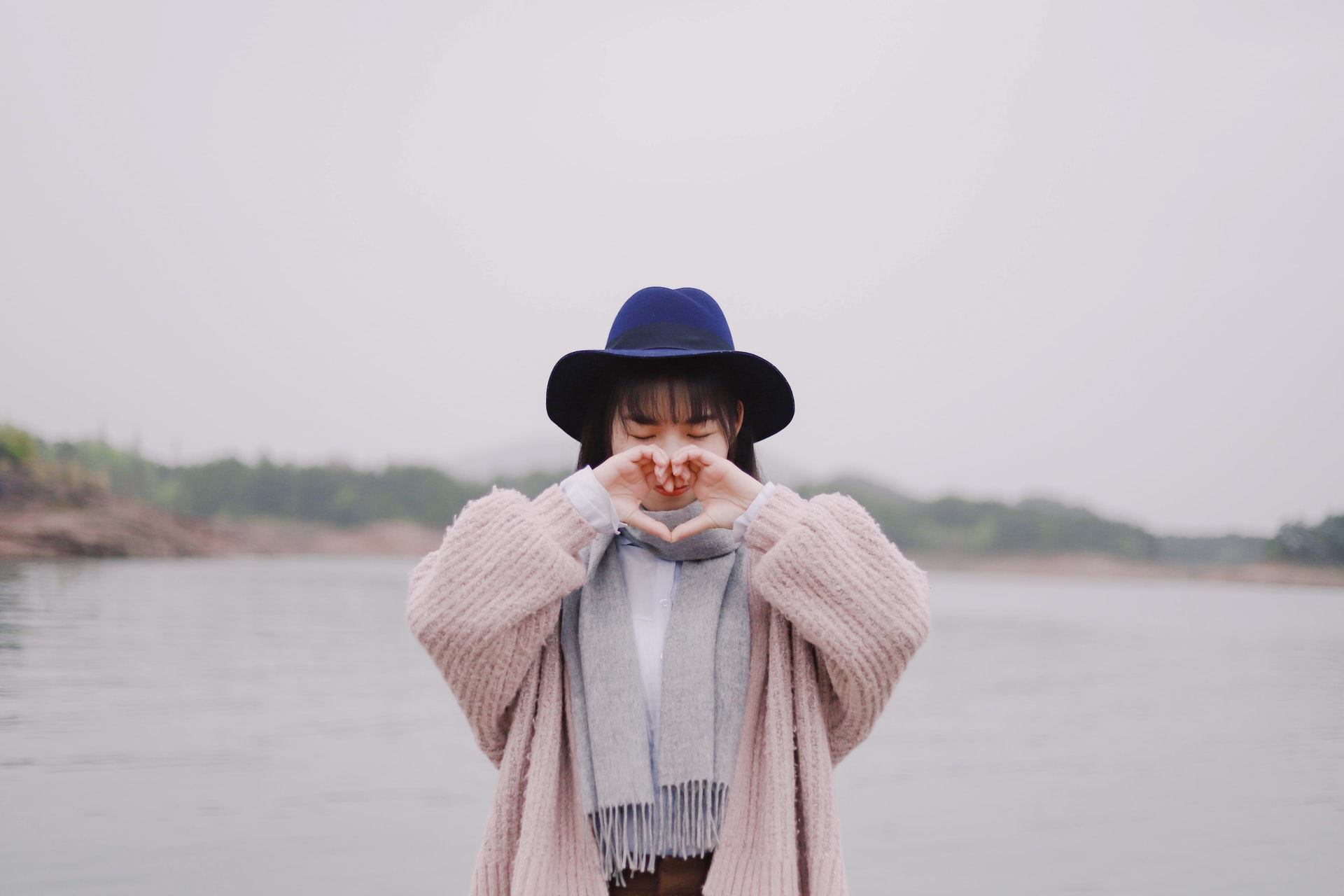 person in pink sweater on beach making heart shape with hands