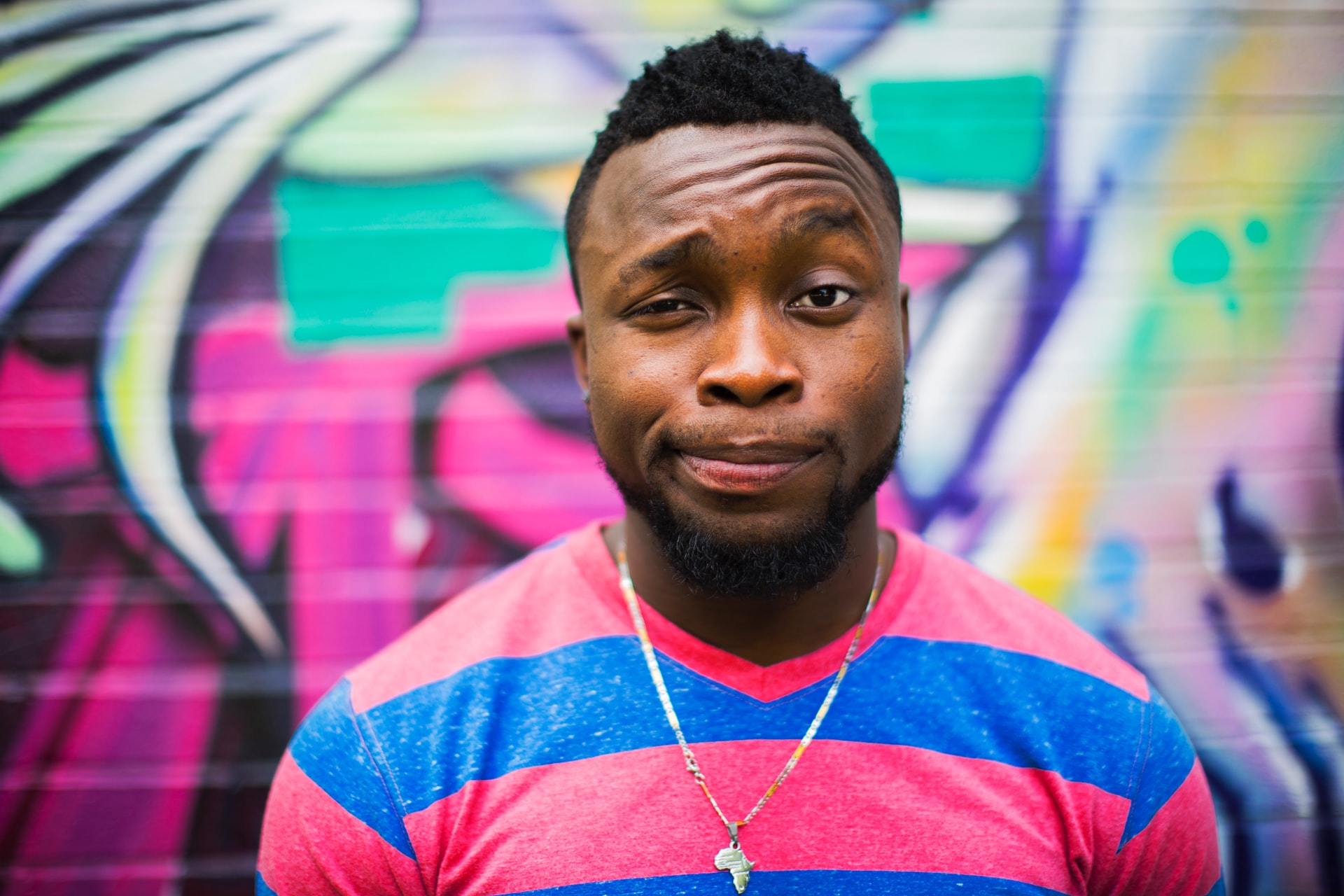 man standing in front of colorful wall making a quizzical face