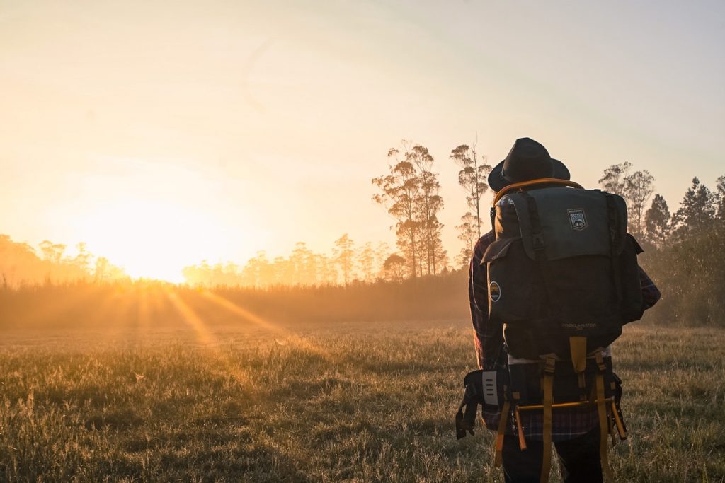 person with backpack hiking towards the sunset