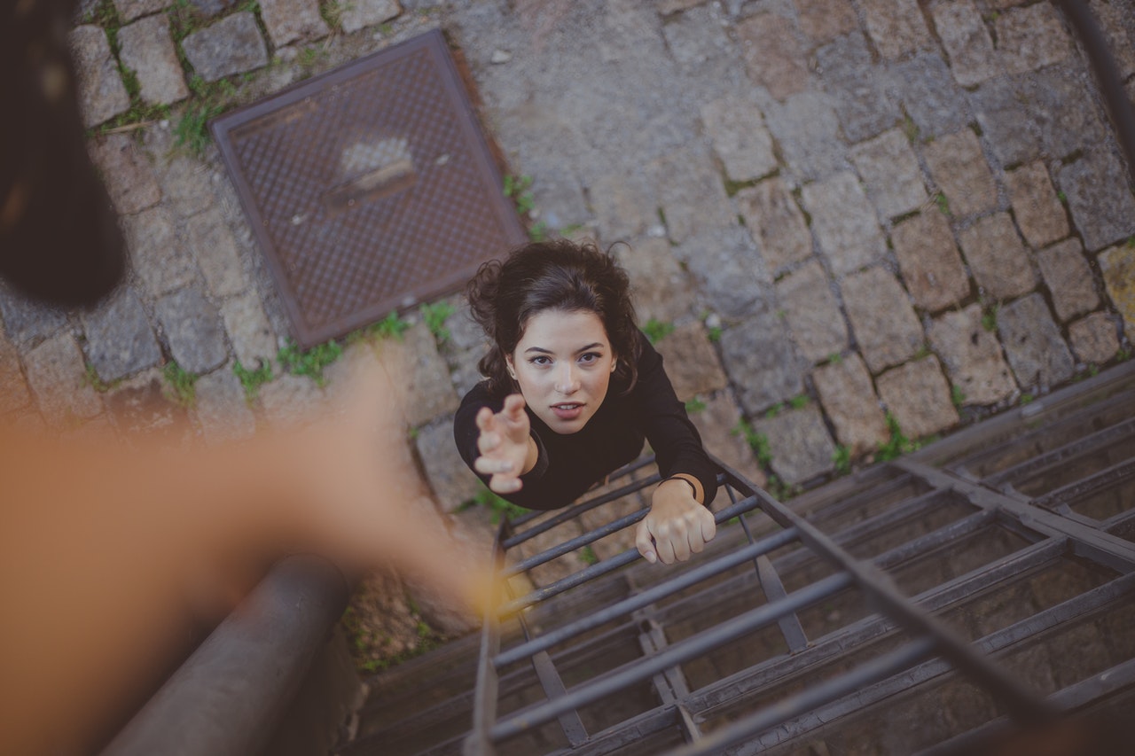 woman climbing a ladder reaching for a helping hand