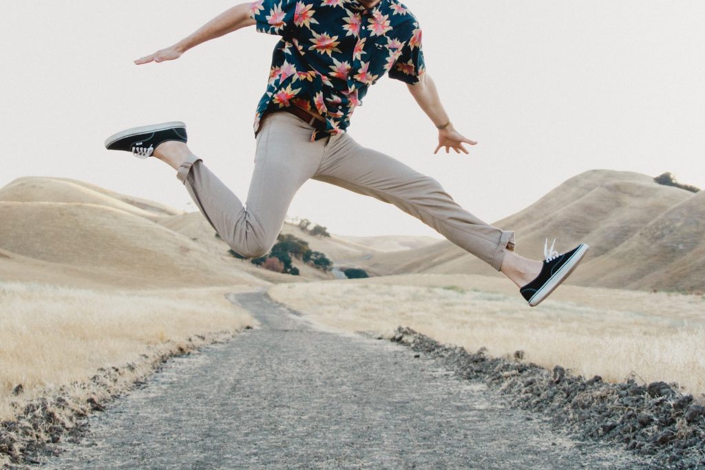 man in floral shirt jumping hills in background