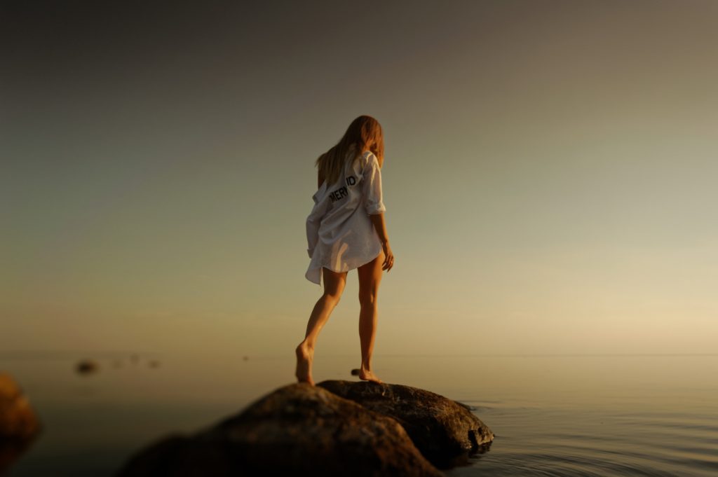 solitary woman walking on rocks by the water
