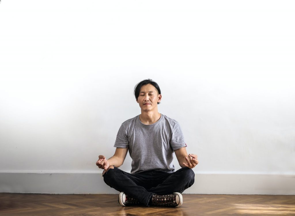 man sitting cross-legged by a white wall meditating