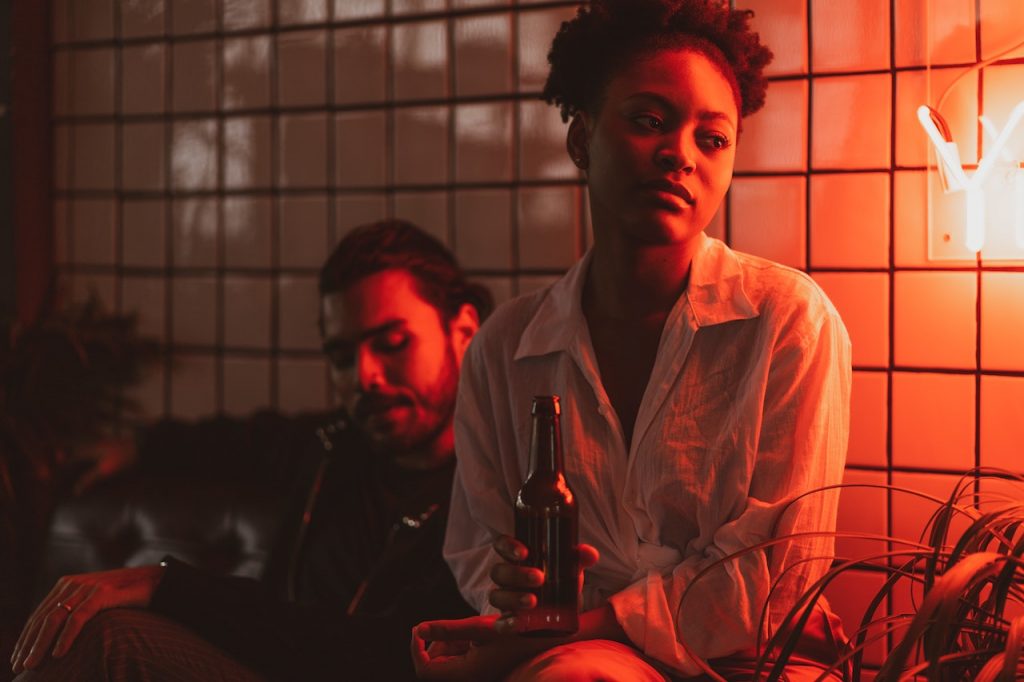 woman sitting in red lit bar with beer looking concerned