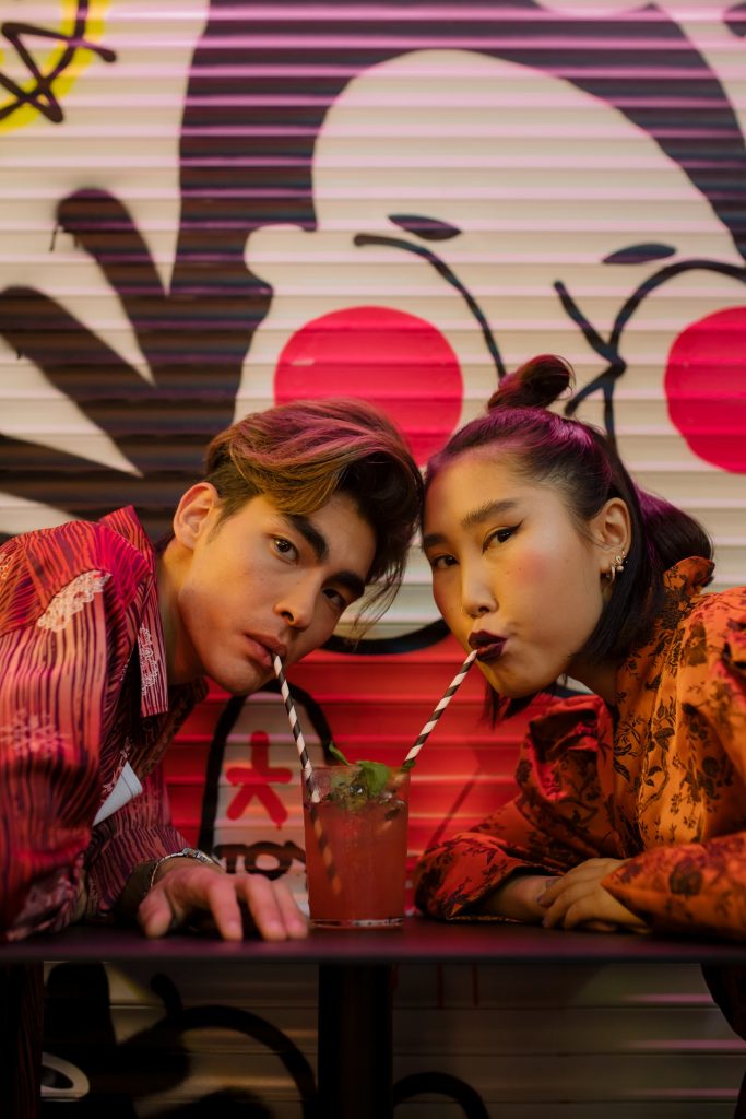 man and woman in similar clothes drinking one cocktail with two straws