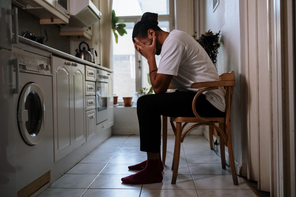 person with head in hands sitting in kitchen