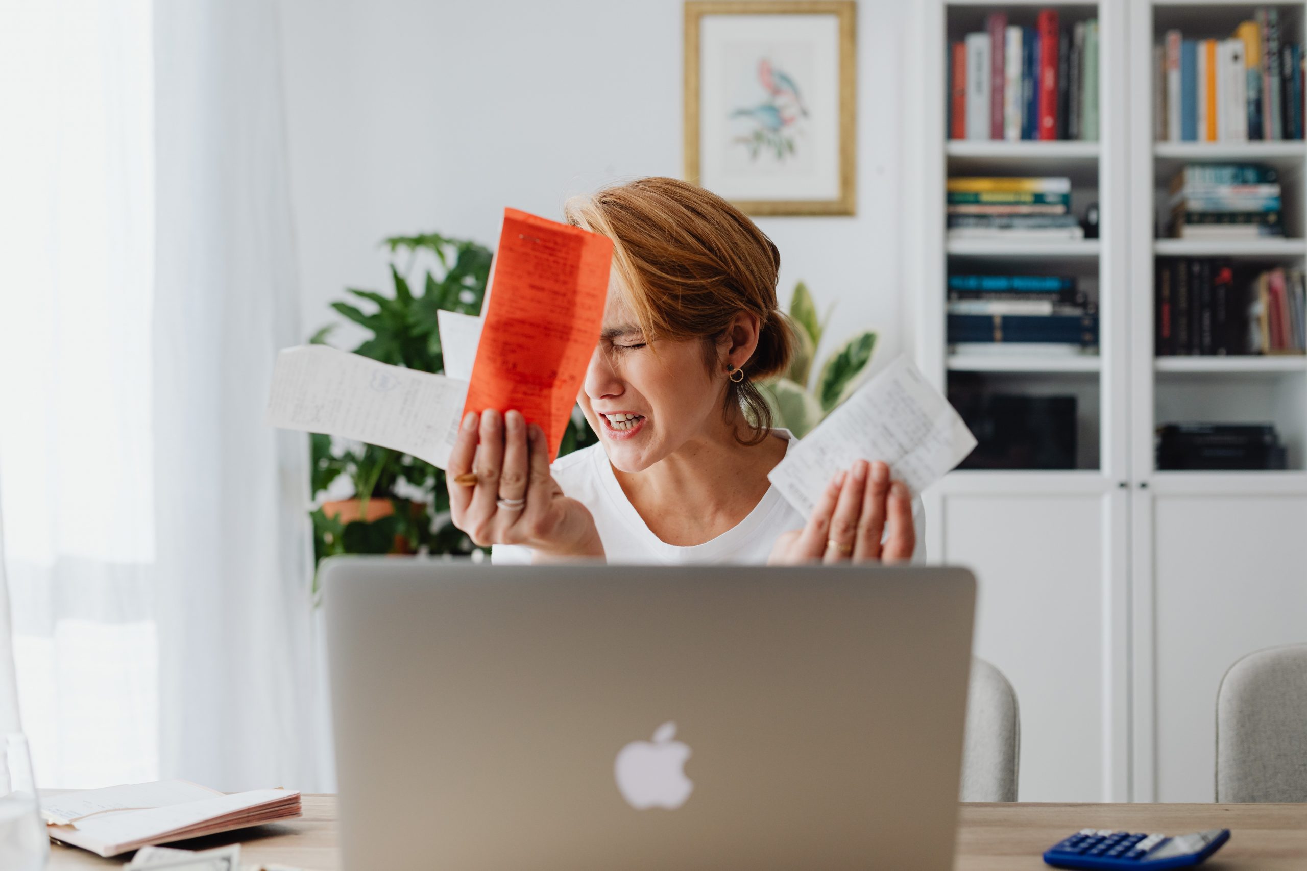 woman holding bills and grimacing in front of computer