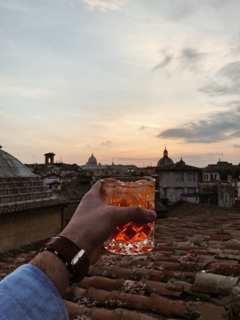 hand holding rocks glass over a rooftop in the evening