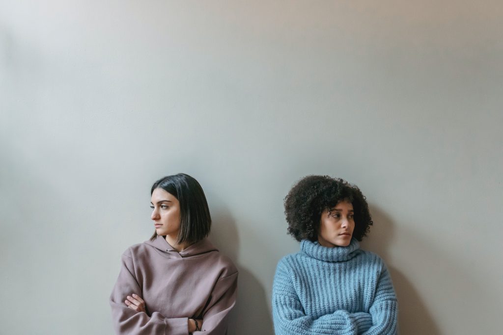 two upset women sitting against a wall looking in opposite directions
