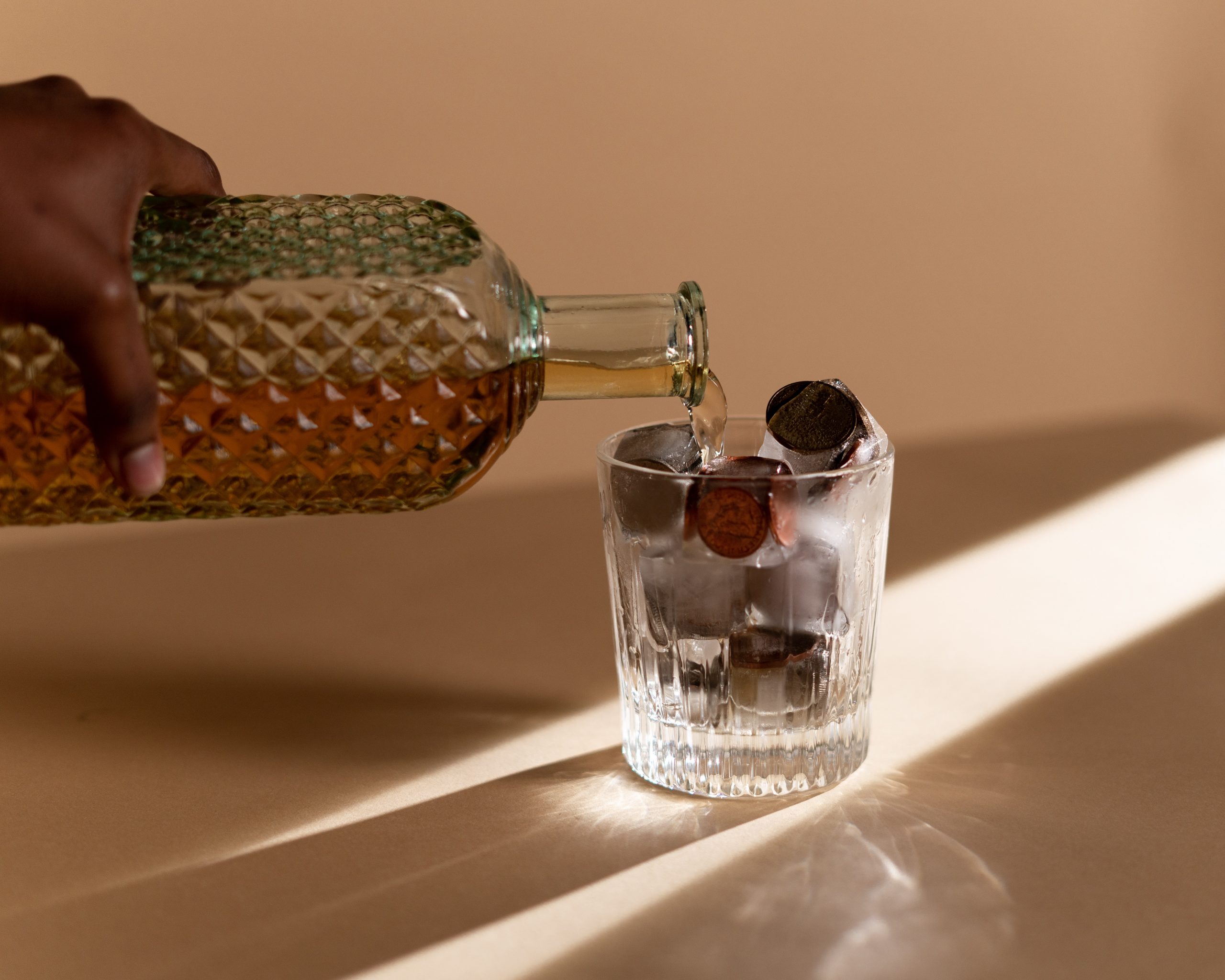 hand pouring liquor into glass full of coins